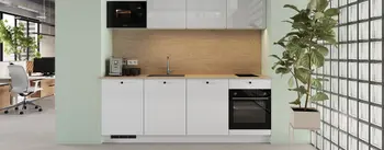 Moderne weiße Einbauküche in mintgrüner Nische mit Holzrückwand, Einbaumikrowelle, Induktionskochfeld, Backofen und Spüle; Kaffeemaschine links, große Zimmerpflanze und Glasbausteinwand rechts; Blick ins offene Büro.